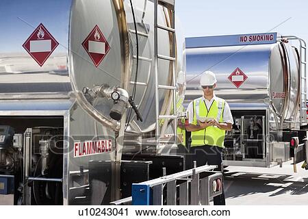 Stock Image - Young male worker using tablet PC by oil tankers. Fotosearch