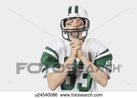 Young man in football uniform with hands clasped standing against gray background View Large Photo Image Stock Photograph - Young man in football uniform with hands clasped standing against gray background. Fotosearch