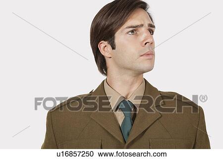 Stock Image - Young man in military uniform looking away against gray background. Fotosearch