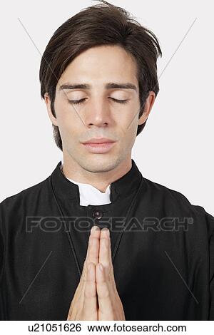Young man in priest costume praying against gray background View Large Photo Image Stock Photograph - Young man in priest costume praying against gray background. Fotosearch