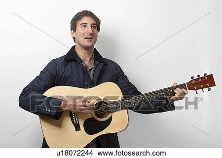 Picture - Young man playing guitar while signing against white background. Fotosearch