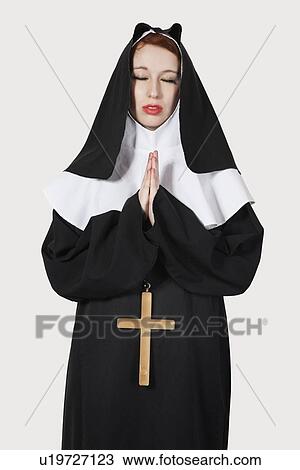 Stock Image - Young nun praying over gray background. Fotosearch