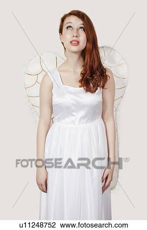 Young woman dressed as an angel looking up against gray background View Large Photo Image Stock Image - Young woman dressed as an angel looking up against gray background. Fotosearch