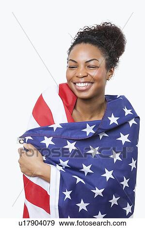 Stock Photo - Cheerful young woman wrapped in American flag over white background. Fotosearch