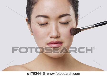 Close-up of young woman applying blush over white background View Large Photo Image Stock Image - Close-up of young woman applying blush over white background. Fotosearch