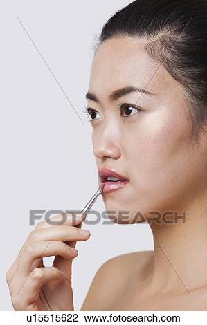 Close-up of young woman applying lip gloss with brush over white background View Large Photo Image Stock Image - Close-up of young woman applying lip gloss with brush over white background. Fotosearch