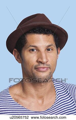 Stock Image - Close-up portrait of young man wearing hat over blue background. Fotosearch