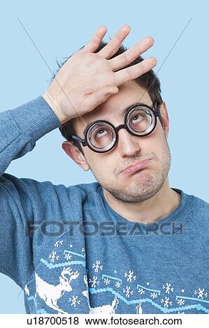 Geek young man wearing novelty glasses with hand on head over blue background View Large Photo Image Stock Photo - Geek young man wearing novelty glasses with hand on head over blue background. Fotosearch