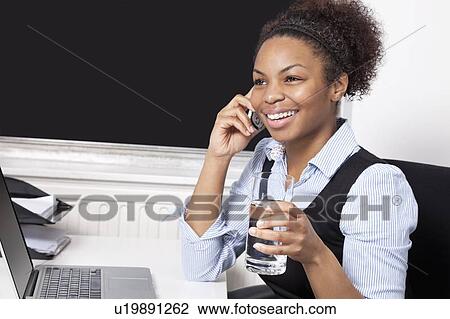 Happy businesswoman using cell phone in front of laptop at desk in office View Large Photo Image Stock Image - Happy businesswoman using cell phone in front of laptop at desk in office. Fotosearch