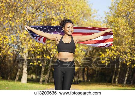 Stock Photograph - Happy young female holding up American flag in park. Fotosearch