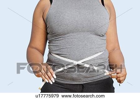 Stock Photo - Mid section of woman measuring waist over blue background. Fotosearch