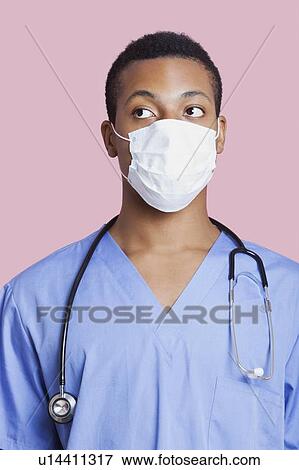 Stock Photo - Mixed race male surgeon wearing surgical mask over pink background. Fotosearch
