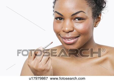 Stock Photo - Portrait of African American young woman applying lip gloss with brush over white background. Fotosearch