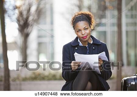 Stock Photo - Portrait of confident African American young woman with documents sitting outdoors. Fotosearch