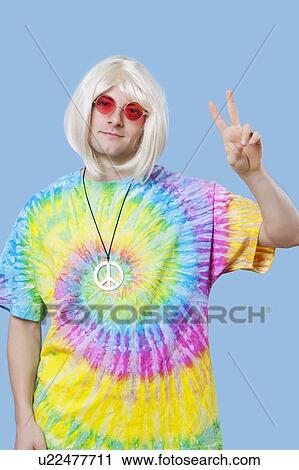 Portrait of funky young man gesturing peace sign against blue background View Large Photo Image Stock Image - Portrait of funky young man gesturing peace sign against blue background. Fotosearch
