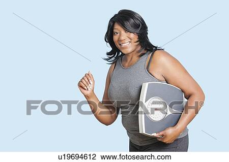 Portrait of happy woman holding scales over blue background View Large Photo Image Stock Image - Portrait of happy woman holding scales over blue background. Fotosearch