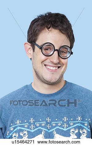 Portrait of happy young man wearing novelty glasses over blue background View Large Photo Image Stock Image - Portrait of happy young man wearing novelty glasses over blue background. Fotosearch