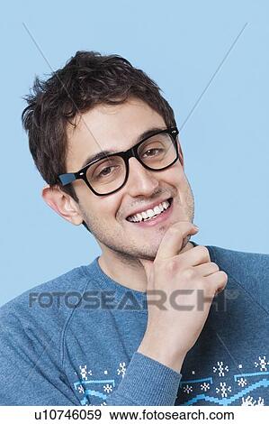 Stock Photo - Portrait of happy young man with hand on chin over blue background. Fotosearch