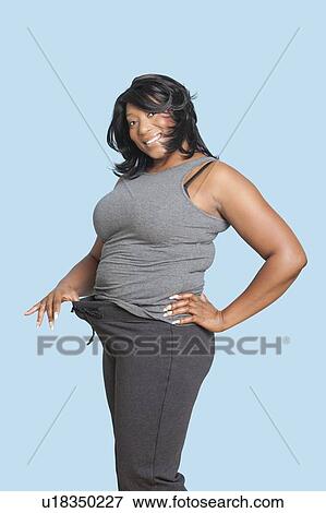 Portrait of mixed race woman pulling put her loose pants waistline over blue background View Large Photo Image Stock Photo - Portrait of mixed race woman pulling put her loose pants waistline over blue background. Fotosearch