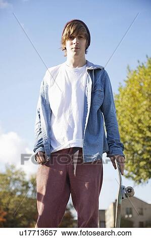 Portrait of serious young man with skateboard against sky View Large Photo Image Stock Photo - Portrait of serious young man with skateboard against sky. Fotosearch