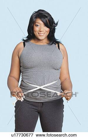 Portrait of smiling mixed race woman measuring waist over blue background View Large Photo Image Stock Photo - Portrait of smiling mixed race woman measuring waist over blue background. Fotosearch