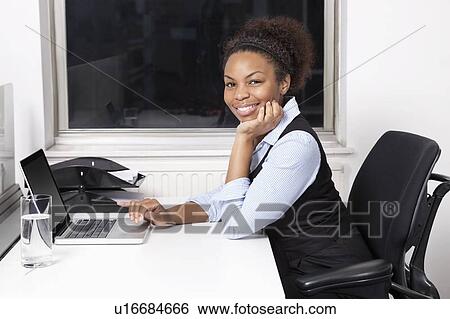 Portrait of smiling young businesswoman using laptop at desk in office View Large Photo Image Stock Photograph - Portrait of smiling young businesswoman using laptop at desk in office. Fotosearch