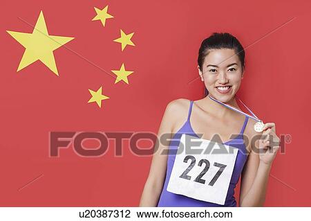 Stock Image - Portrait of smiling young female medalist standing against Chinese flag. Fotosearch