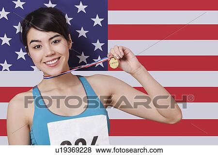 Stock Photo - Portrait of smiling young female medalist standing against American flag. Fotosearch