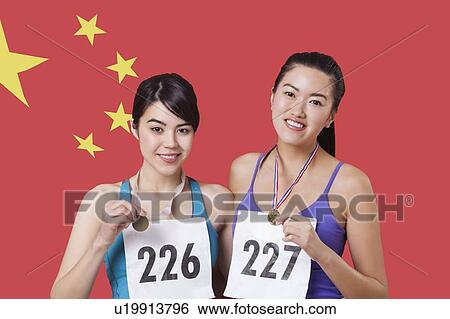 Stock Photograph - Portrait of smiling young medalists standing against Chinese flag. Fotosearch