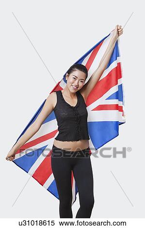 Stock Photography - Portrait of smiling young woman holding British flag over white background. Fotosearch