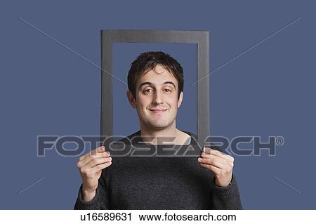Portrait of young man smiling through frame over blue background View Large Photo Image Stock Image - Portrait of young man smiling through frame over blue background. Fotosearch