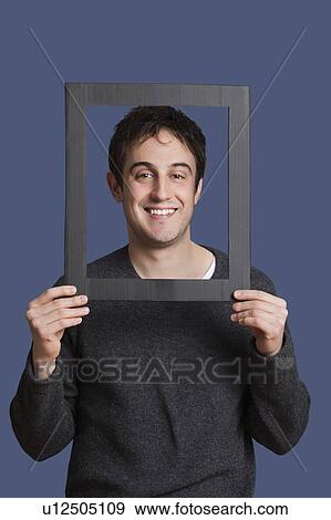 Portrait of young man smiling through frame over blue background View Large Photo Image Stock Photo - Portrait of young man smiling through frame over blue background. Fotosearch