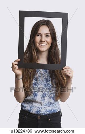 Portrait of young woman smiling through frame over white background View Large Photo Image Stock Photograph - Portrait of young woman smiling through frame over white background. Fotosearch