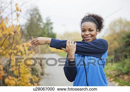 Stock Image - Portrait of young woman stretching in park. Fotosearch