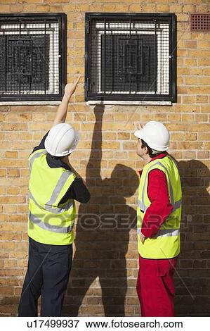 Rear view of two male worker in hardhats pointing towards windows View Large Photo Image Stock Photo - Rear view of two male worker in hardhats pointing towards windows. Fotosearch