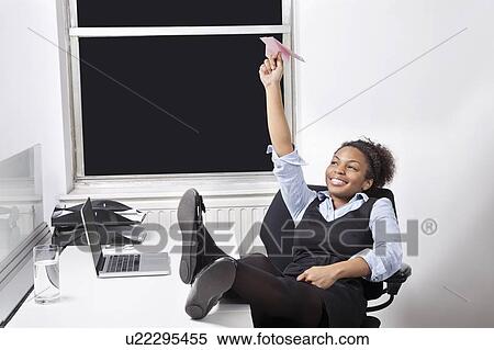 Stock Photography - Relaxed businesswoman throwing paper airplane in office. Fotosearch