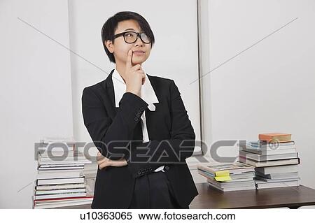 Stock Photography - Thoughtful young businesswoman with stack of books on desk in office. Fotosearch