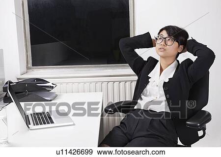 Stock Photo - Young businesswoman resting on chair in front of laptop in office. Fotosearch