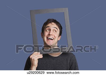 Young man laughing through frame over blue background View Large Photo Image Stock Photo - Young man laughing through frame over blue background. Fotosearch