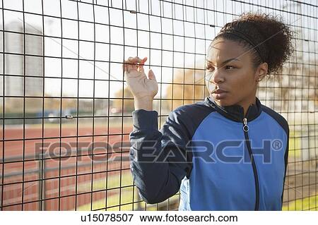 Young woman in sports jacket looking away through net at park View Large Photo Image Stock Photo - Young woman in sports jacket looking away through net at park. Fotosearch