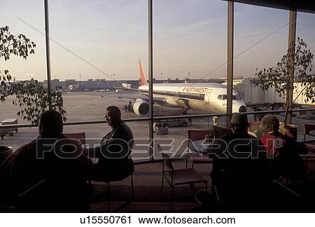 Stock Image -  airport, terminal, Pennsylvania, Philadelphia, People waiting in airport terminal at Northwest gate at the Philadelphia International Airport in Philadelphia in the state of Pennsylvania. Northwest plane seen from the window of the terminal sitting outsi. Fotosearch