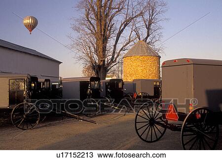 Stock Image -  amish, buggy, farm, hot air balloon, Amish Country, Lancaster County, Pennsylvania, Amish buggies are parked outside and Amish farm while a hot air balloon rises in the background in Pennsylvania Dutch Country in the state of Pennsylvania.. Fotosearch