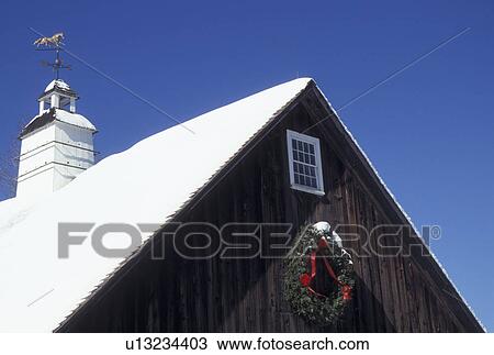 Stock Image -  barn, Vermont, VT, Top of a brown barn with weathervane decorated with a wreath in the snow in winter in Pomfret.. Fotosearch
