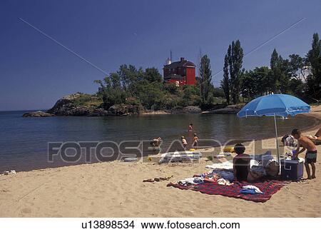 beach, Lake Superior, Upper Peninsula, U. P Michigan, People enjoying a day in the sun at Shiras Park Beach with red lighthouse and coast guard station in the distance on Lake Superior in Marquette in the state of Michigan. View Large Photo Image Picture - beach, Lake Superior, Upper Peninsula, U. P Michigan, People enjoying a day in the sun at Shiras Park Beach with red lighthouse and coast guard station in the distance on Lake Superior in Marquette in the state of Michigan.. Fotosearch