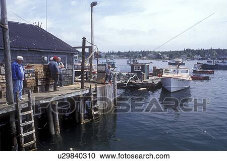 Stock Image -  Bernard, Maine, Mount Desert Island, Atlantic Ocean, Fishermen standing next to lobster traps on the wharf. Fishing boats are docked in Bass Harbor. . Fotosearch