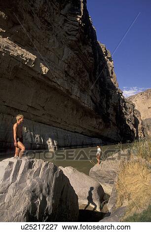 Stock Photo -  Big Bend National Park, Rio Grande, river, canyon, Texas, A couple of hikers standing on boulders next to the Rio Grande on U. S. and Mexico border in Santa Helena Canyon at Big Bend National Park. Fotosearch