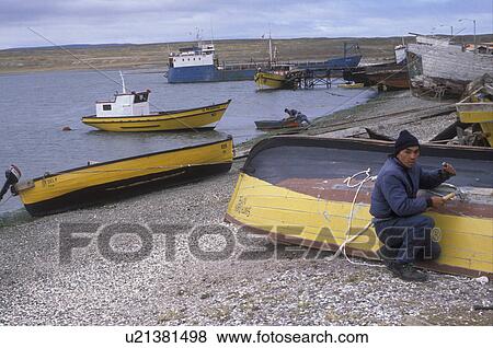 Stock Photo -  boats, Patagonia, Tierra del Fuego, Chile, Man repairing fishing boats on the shore of the Strait of Magellan in the harbor town of Porvenir in Chile.. Fotosearch