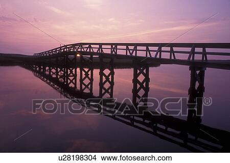 Picture -  bridge, Cape Cod, Sandwich, Massachusetts, Atlantic Ocean, The sunrises over the inlet. The silhouette of the board walk reflects in the water of Cape Cod Bay.. Fotosearch