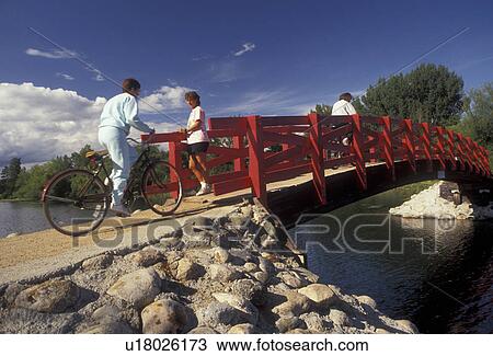 Stock Image -  bridge, Minnesota, People [walking, biking] across a red bridge which crosses over the Fish Hook River in Park Rapids in the state of Minnesota.. Fotosearch