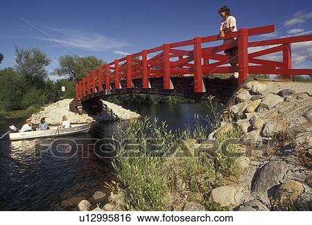 Stock Photograph -  bridge, Minnesota, Woman standing on a red bridge which crosses over the Fish Hook River watching people cruise by in a boat in Park Rapids in the state of Minnesota . Fotosearch